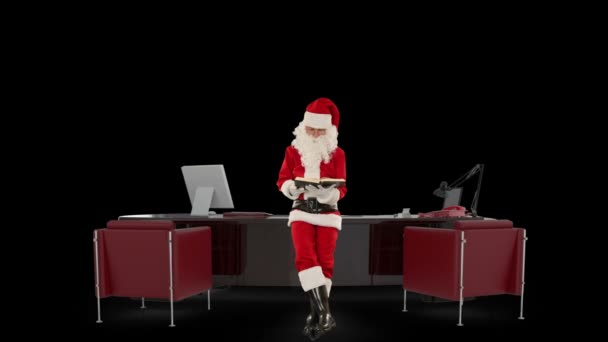 Santa claus lezen van een boek in zijn moderne kerst kantoor, tegen zwart — Stockvideo