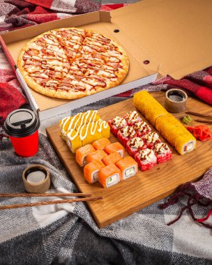 Pizza, menü için suşi fotoğrafı. Evin sıcacık battaniyelerinde akşam yemeği. Salgın sırasında suşi ve pizza teslimatı. Ekmek ve pizza seti.
