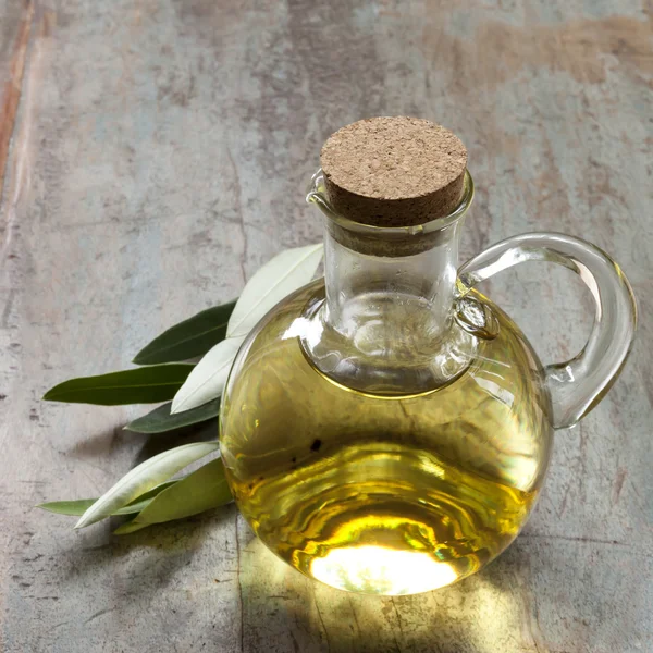Aceite de oliva y hojas de aceituna sobre madera rústica — Foto de Stock