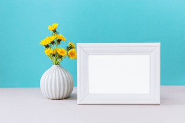 Beyaz çerçeveli, vazoda yabani sarı karahindiba çiçekleri olan bir resim. Sunum tasarımı için boş çerçeve modeli. Aralık arkaplanındaki beyaz şablon
