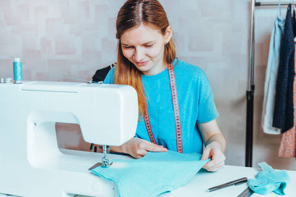 Портной женского пола создаёт шаблон. Молодая улыбающаяся модельер работает за столом на швейной машинке. Платье делает одежду на своем рабочем месте. Шитье как концепция малого бизнеса
