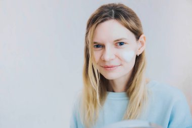 Çekici bir genç kadının portresi evde yüzüne nemlendirici sürüyor. Cilt bakımı, cilt temizleme, köpük ve cilt temizleme krem, kozmetoloji ve ev cilt bakımı ile nemlendirici.