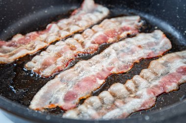 Kızarmış domuz pastırması dilimi ya da striptiz. Sağlıksız yağlı yiyecekler, şişmanlatıcı malzemeler. Kırmızı ince dilimler ya da pastırma kızartmaları tavada kızartılır, domuz yağı eritilir. Yüksek kalorili yiyecekler. Kahvaltı fikri..