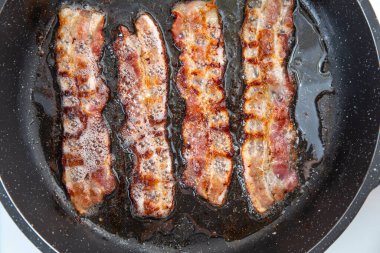 Kızarmış domuz pastırması dilimi ya da striptiz. Sağlıksız yağlı yiyecekler, şişmanlatıcı malzemeler. Kırmızı ince dilimler ya da pastırma kızartmaları tavada kızartılır, domuz yağı eritilir. Yüksek kalorili yiyecekler. Kahvaltı fikri..