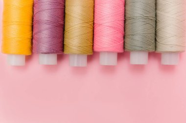 Zarif pembe arka planda dikiş aletleri ve dikiş aksesuarları. Terzilik, terzilik. Çok renkli dikiş iplikleri, iplik makaraları, iğneler, iğneler. Üst manzara, terzi işi için düz yatak..