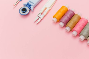 Zarif pembe arka planda dikiş aletleri ve dikiş aksesuarları. Terzilik, terzilik. Çok renkli dikiş iplikleri, iplik makaraları, iğneler, makas. Üst manzara, terzi işi için düz yatak..