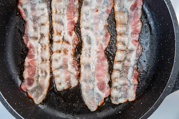 Crispy smokey fried bacon slice or strip. Unhealthy fat food, fattenig ingredient. Red Thin slice or strip or rashers of bacon is fried in a pan, pork fat is melted. High calorie food. Breakfast idea.