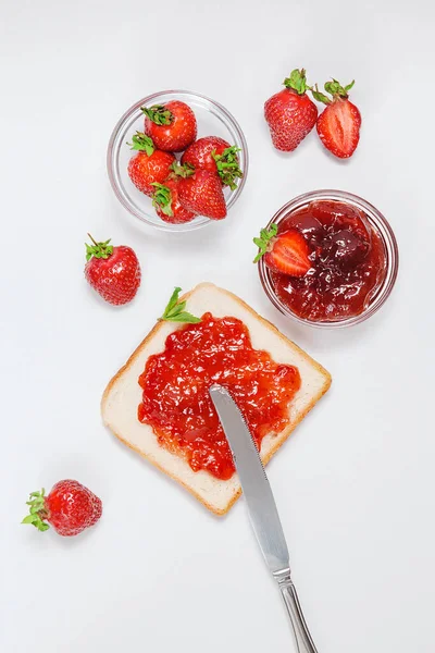 烤着草莓果酱做早餐 背景是白色的 顶部视图 成熟的新鲜草莓和自制草莓果酱 用刀铺在面包上 — 图库照片