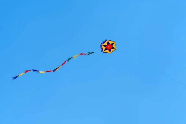 Renkli yuvarlak bir uçurtma gökyüzünde yükselir Mavi gökyüzünde. Spor uçurtma festivali. Yunanistan 'da temiz bir pazartesi. Kıvrılan kuyruklu uçan bir uçurtma. Kopyalama alanı