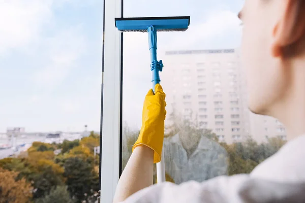 Man in yellow gloves cleaning window with squeegee and spray detergent at home terrace. House cleaning and house chores, domestic hygiene. Window cleaning background with blue sky