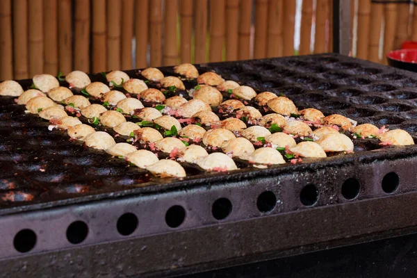 Japanese street food takoyaki at special grill pan. Process of cooking takoyaki balls with octopus filling. Japanese snacks and street food at the festival