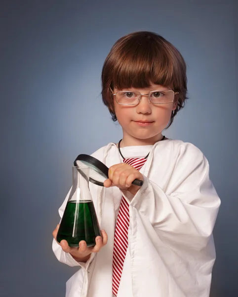 Pojke studera ett ämne i ett provrör med förstoringsglas — Stockfoto