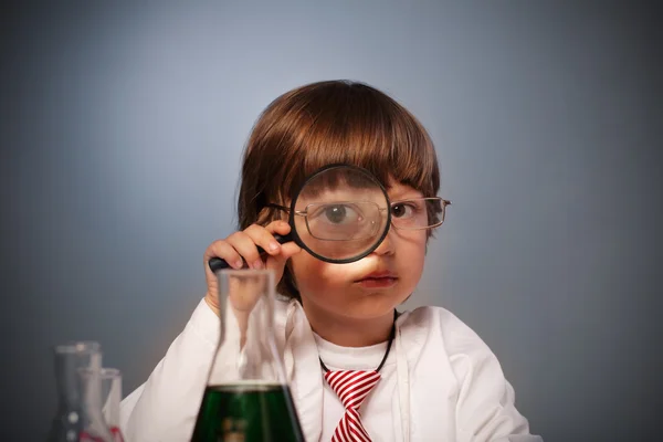 Junge untersucht Substanz im Reagenzglas mit der Lupe — Stockfoto