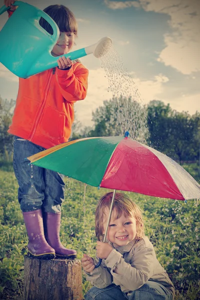 İki kardeş dışarıda yağmur altında oynuyorlar. — Stok fotoğraf