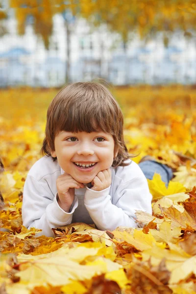 Mutlu çocuk sonbahar yapraklarının içinde yatıyor — Stok fotoğraf