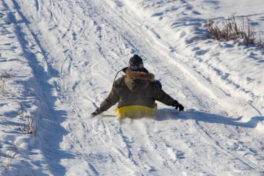 Oğlan kışın kızakla kar tepesinden kayıyor, kızakla kayıyor ve mevsim konseptini anlatıyor.