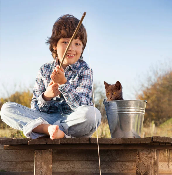 湖の岸に釣り竿とペット つの子供とフィッシャーの子猫と川に釣りに行く幸せな少年 ストック写真