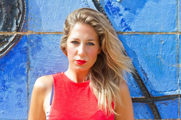 Mavi duvarın önünde duran genç bir kadının portresi.