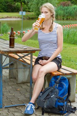 Genç bir kadın gölde buğday birası içiyor.