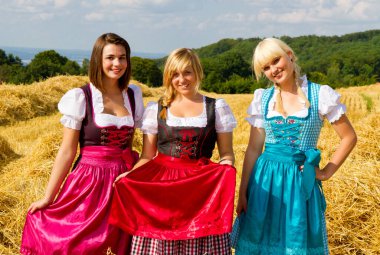 Bir tarlada renkli dirsekler içinde üç mutlu kız.