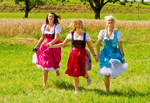 Three girls in dirndls running over a meadow