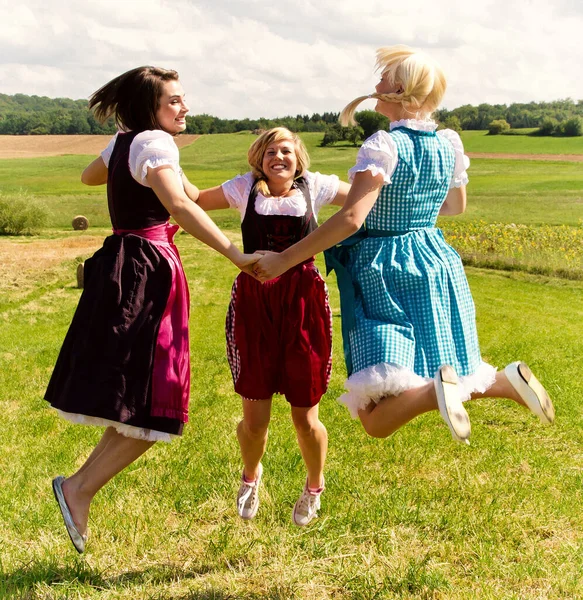 Three Happy Girls Dirndls Jumping Meadow —  Fotos de Stock