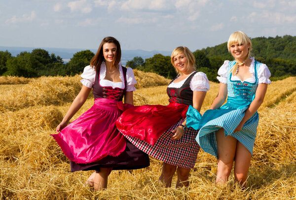 Three happy girls in colorful dirndls on a field