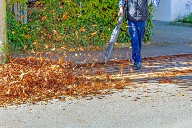 Worker on a street in autumn with a leaf blower