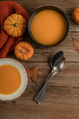 Kış kabağı ve sonbahar yapraklarıyla süslenmiş ahşap masada iki kase balkabağı çorbası.