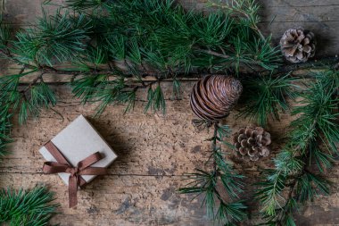 Noel arkaplanı, Noel hediye kutusu, çam ağacı dalı ve tahta masanın üzerindeki koniler. Noel veya yeni yıl için kopya alanı olan ahşap yüzeyde en üstteki görünüm hediye kutusu