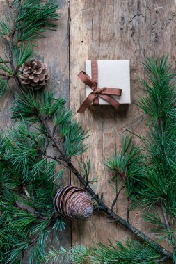 Noel hediyesi kutusu, köknar ya da Noel ağacı dalı ve tahta arka planda çam kozalakları. Noel veya yeni yıl için kopya alanı olan ahşap yüzeyde en üstteki görünüm hediye kutusu