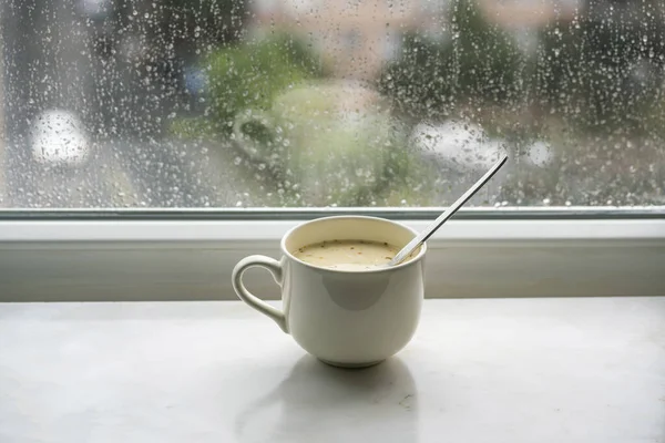 スープ雨の日に窓辺のボウルに自家製スープ 窓ガラスに雨が降る 雨が降っている間に窓によって選択的に焦点を当てたマグカップやカップ ストック画像