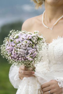 Gelin çiçeği, gelinin eli açık havada çiçek buketi tutuyor. Gürültü efektleri olan ve bukete özel bir odak noktası olan klasik gelinlik giyen bir kadının vücudu.. 