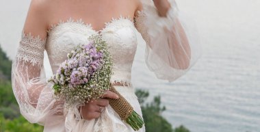 Gelin çiçeği, gelinin eli açık havada çiçek buketi tutuyor. Seçici odaklı klasik gelinlik giyen bir kadının vücudu.. 