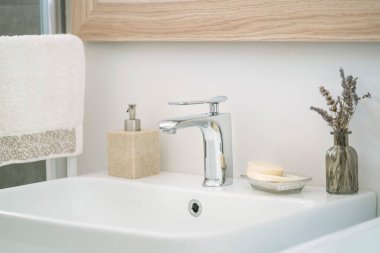 Banyo, asılmış havlu ve ev içi tuvalette beyaz lavabo ve sıvı sabun şişesi. Musluklar ve sabunlar beyaz ve temiz lavaboda seçici odak ve gürültü efektleriyle