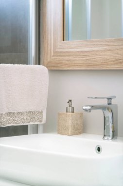 Banyo, asılmış havlu ve ev içi tuvalette beyaz lavabo ve sıvı sabun şişesi. Musluklar ve sabunlar beyaz ve temiz lavaboda seçici odak ve gürültü efektleriyle