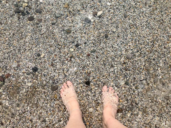 小さな小石や岩で海に立って白い白人女性の美しい足を表示します 穏やかな海と夏の休日の背景の概念写真はコピースペースを持っています — ストック写真