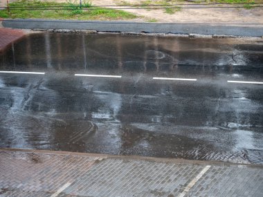 Şiddetli yağmur damlaları sağanak yağış sırasında şehir caddesine, boş park alanına ve su birikintileri olan yola düşüyor.