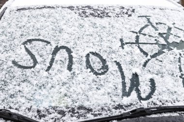 The inscription snow, on the surface of the car front windshield, covered with snow
