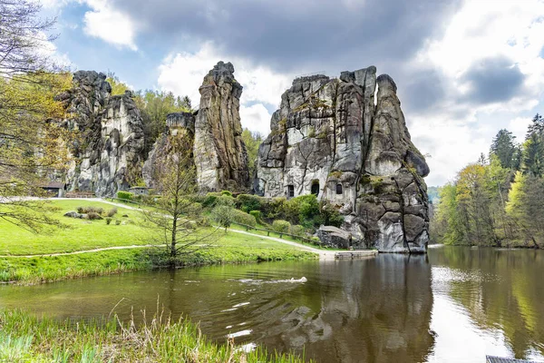 The dog swims in the lake near unique rock formation Externsteine near Detmold, Nordrhein-Westfalen, Teutoburger Wald, Germany, view from the side of the lake