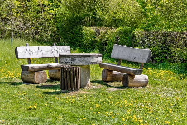 Tahta banklar ve çimento masa çalıların arasında çiçek açan karahindiba çayırlarının üzerinde.