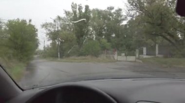 Şoför yağmurda araba kullanıyor. Arabada kötü hava var. Ön camda çatlak var.