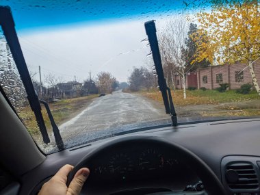 Arabanın camında yağmur damlaları var. Arabayı kapıya doğru sür. Kötü havada seyahat etmek. Sürücü direksiyonda. 