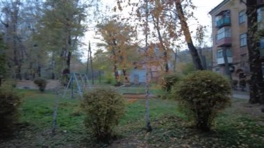 Modern yerleşim alanı olan şehir manzarası, yeni apartmanlar ve sonbaharda yaya geçidi ve ağaçları olan yeşil avlu. Bahçede sonbahar yaprakları. Eski evin avlusunda yürü.