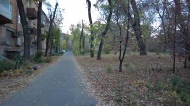 Modern yerleşim alanı olan şehir manzarası, yeni apartmanlar ve sonbaharda yaya geçidi ve ağaçları olan yeşil avlu. Bahçede sonbahar yaprakları. Eski evin avlusunda yürü.