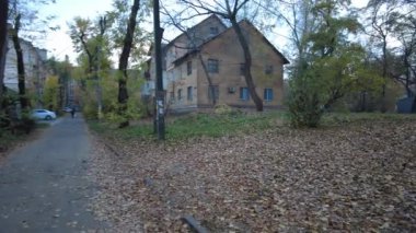 Modern yerleşim alanı olan şehir manzarası, yeni apartmanlar ve sonbaharda yaya geçidi ve ağaçları olan yeşil avlu. Bahçede sonbahar yaprakları. Eski evin avlusunda yürü.
