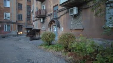 Modern yerleşim alanı olan şehir manzarası, yeni apartmanlar ve sonbaharda yaya geçidi ve ağaçları olan yeşil avlu. Bahçede sonbahar yaprakları. Eski evin avlusunda yürü.