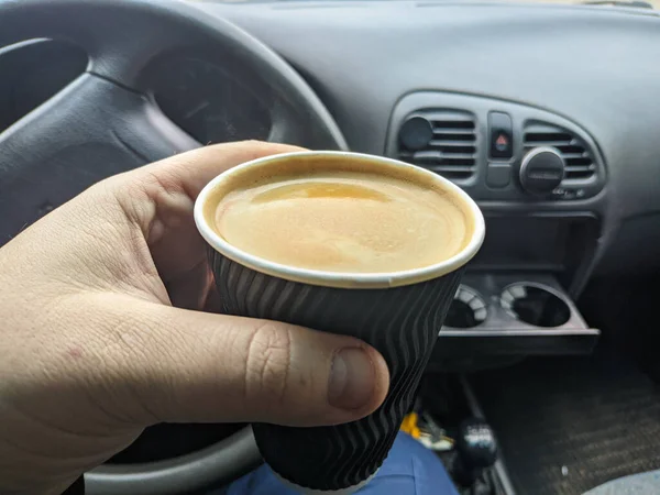 車の中のコーヒー 男は車の中でコーヒーペーパーカップを保持 コーヒーは旅行者の友人です 交通と車両のコンセプト 車を運転しながらコーヒーを飲む男 コーヒーブレイク — ストック写真