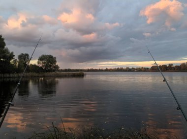 Nehirde balık tutmak. Elinde olta olan bir balıkçı. Yakalayın. Olta kamışı tekeri yakın çekim, gün doğumuyla balık tutma. Elinde olta ve kova olan küçük bir kız balık tutmaya geldi ve gölete baktı..