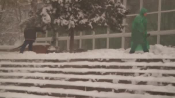人们铲雪 台阶上的雪 男人和女人拿着铲子 暴风雪 坏天气 模糊的背景 — 图库视频影像